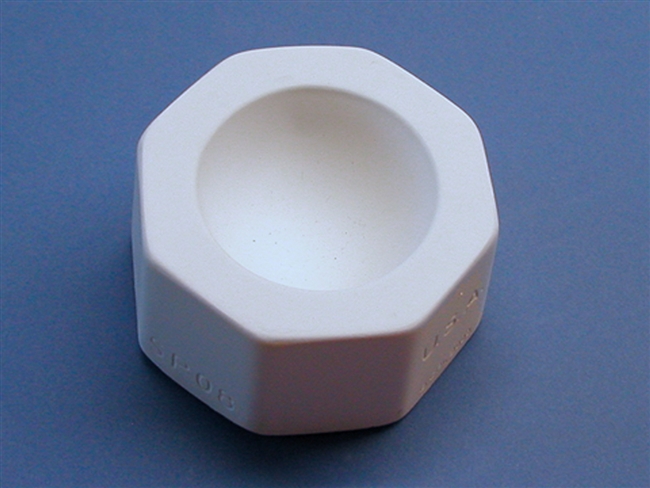 A white plaster mold for pressing moist clay into shapes on a blue background. It is octagonal in shape. A small inverted circular dome is carved into the center.