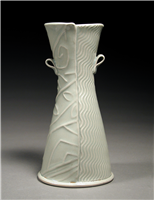 An hourglass shaped vase made of ceramic. It is divided into two halves vertically. The left half is textured with widely spaced geometric designs and the right with thinly spaced symmetrical repeating waves. It has two small looped handles.