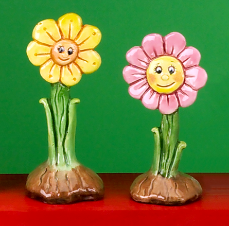 Two cast ceramic figures made to look like flowers sprouting from piles of dirt. Each flower has a long stem with two long leaves. Both have cartoonish faces in the center. The right has a larger flower and leans slightly left.