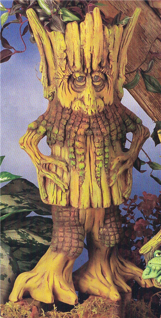 A cast ceramic figure of a tall, cartoonish, ent like creature, appearing to be made of wood. Its separate head is a planter, with bent stick arms on either side. It has a face with large nose and beard like bark. It is placed atop legs with wide feet.
