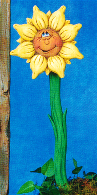 A two part cast ceramic garden stake shaped like a sunflower with a cartoonish face. The slightly curved stem has two small side leaves. The flower looks up with a wide smile. It has large teardrop shaped petals with smaller ones between.