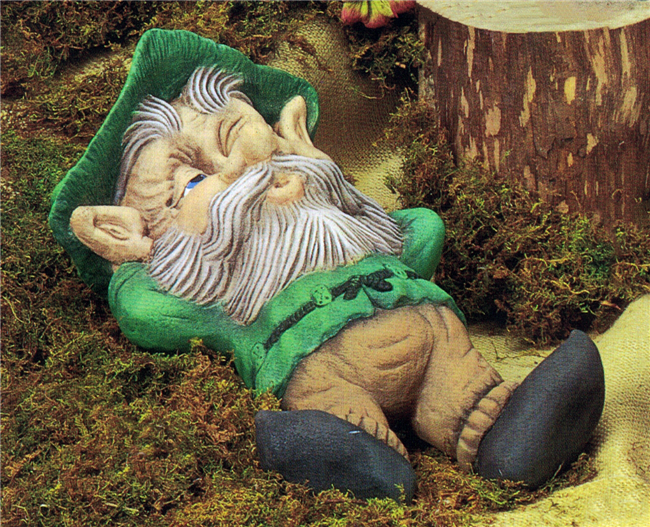 A large cast ceramic figure of a cartoonish gnome. He has a large nose and ears, wears a cap, and has long facial hair. He lays on his back, arms behind his head, eyes just barely open.