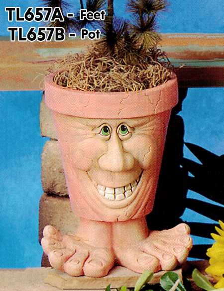 A cast ceramic pot with a cartoonish human face. It wears a large grin with visible teeth and small, closely spaced eyes. The pot is textured with a few small lines like aged cracks. It is placed atop wide cartoonish cast ceramic feet to support it.