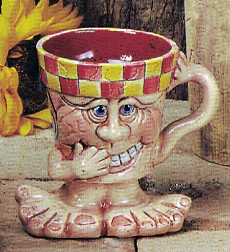 A cast ceramic cup. It has a cartoonish human face and a base of wide, cartoonish feet. One small arm is raised to its mouth while the other extends out and up and serves at the cup handle. The face wears a wide, toothy grin, as if laughing.