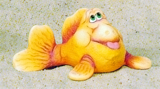 A cast ceramic figure of a cartoonishly styled fish with a humorous expression. It gazes upwards with its tongue sticking out. It is posed with its tail slightly to one side and its pectoral fins in front of it, flat against the ground.