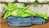 A cast ceramic figure of a cartoonishly styled frog laying on its side atop a worn plank of wood. The frog supports its head with one arm and has its ankles crossed. The word WELCOME is carved into the plank below it as it looks forward with a smile.