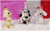 Three separate small cast ceramic figures of cartoonishly styled dog ornaments. The left stands, begging, with a hoop on its head. The middle sits with a bone in its mouth and one on its head. The right sits with long ears splayed to the side and a bow.