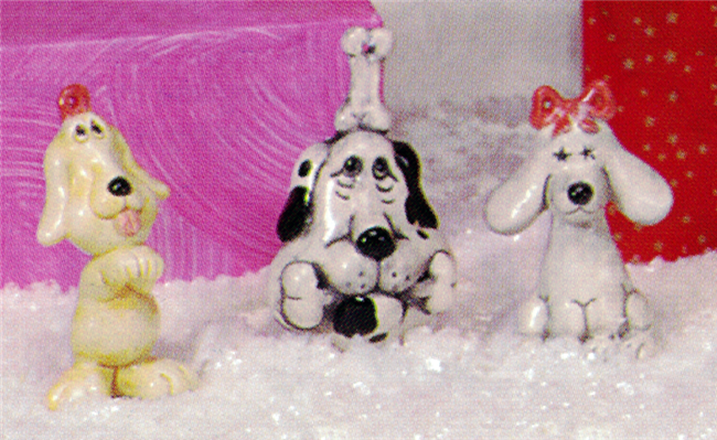 Three separate small cast ceramic figures of cartoonishly styled dog ornaments. The left stands, begging, with a hoop on its head. The middle sits with a bone in its mouth and one on its head. The right sits with long ears splayed to the side and a bow.