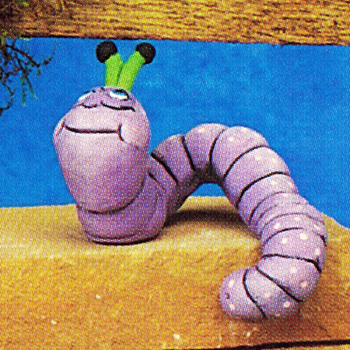 A cast ceramic figure of a cartoonish caterpillar. It has visible body segments and two stocky antennae. Its head looks up as its body curls around and its tail points down. It has a wide smile.