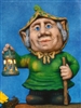 A cast ceramic figure made of multiple pieces assembled into a cartoonish elderly gnome woman. She has a large nose and ears and wears a bonnet. She holds a lantern in her outstretched right hand and a walking stick in her left.