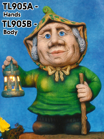 A cast ceramic figure made of multiple pieces assembled into a cartoonish elderly gnome woman. She has a large nose and ears and wears a bonnet. She holds a lantern in her outstretched right hand and a walking stick in her left.