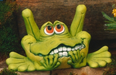 A cast ceramic statue of a cartoonish frog. It sits, bent back legs protruding well above its head. It looks up with large eyes and a nervous, toothy mouth. Its hands are to its mouth as if chewing its nails.