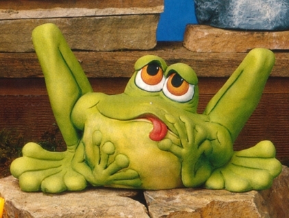A cast ceramic statue of a cartoonish frog. It sits, bent back legs protruding well above its head. It looks upward with lidded eyes, its head tilted. It sticks its tongue out slightly, and holds its face in its hands.