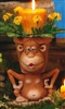 A cast ceramic pot made to resemble a cartoonish monkey. Its head forms the pot, with the rim just visible behind its forehead and round ears. It looks forward, lips pursed and open. It is seated with arms bent and held upward, hands at its sides.
