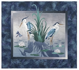 Quilt block of two blue herons standing in a pond, surrounded by lily pads and a dragonfly.