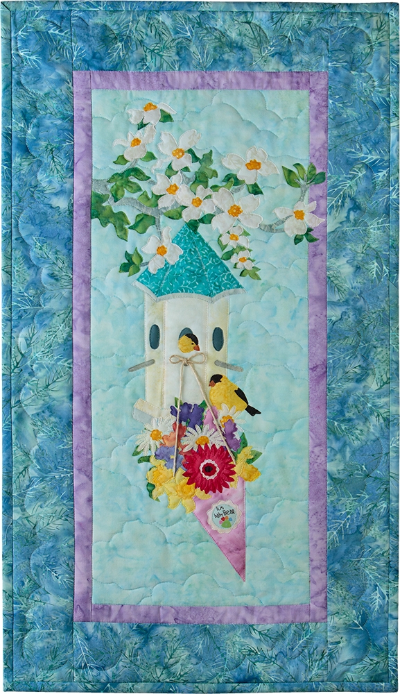 A bird house hanging on a flowering tree branch, with a bouquet of beautiful, colorful flowers hanging off the front. Two small yellow birds are sitting on the flowers and in the bird house.