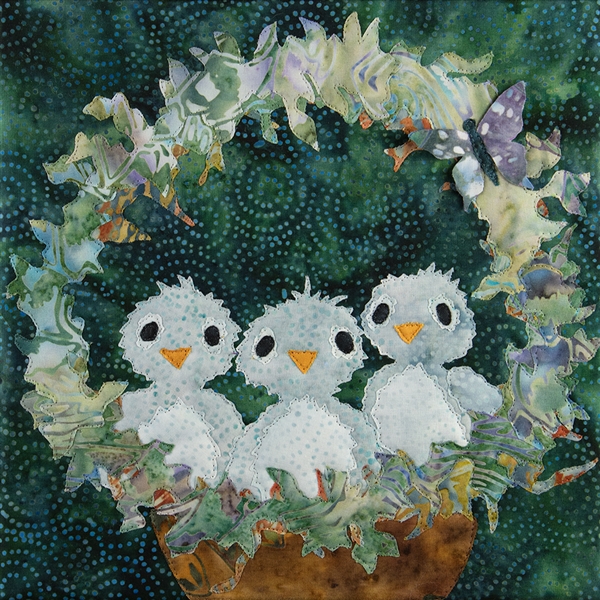 A quilt block with three baby blue birds sitting in their nest with sweet expressions on their faces. A little butterfly is on the arch over the nest.