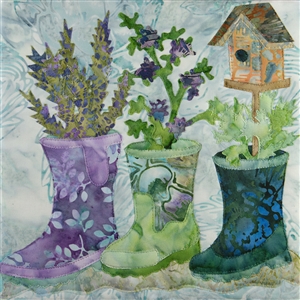 A quilt block with three rain boots that have been converted into planters. One boot also has a bird house on a stand coming out of it