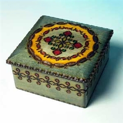 This square box is decorated with a circular pattern around a cross. Yellow, red, and green accents enhance the antiqued look of the box and a lip around the lid distinguishes the carving around the side of the box.