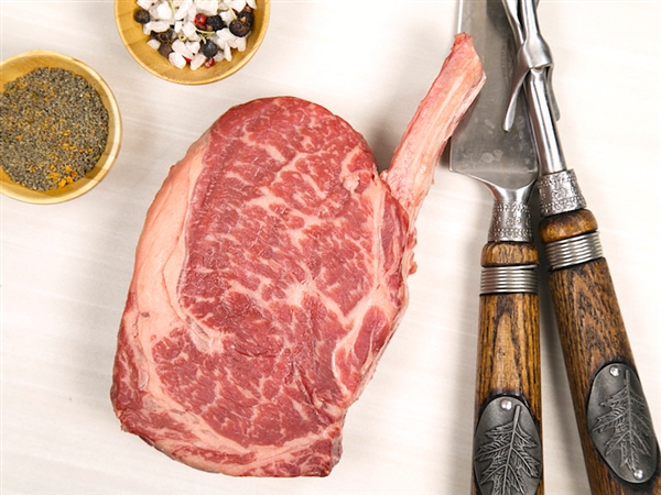 A tall, thick bacon-wrapped filet mignon on a platter alongside a marbled Black Angus ribeye.