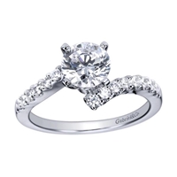 A single diamond row swirls towards a round center diamond in this sleek and stylish white gold or platinum diamond engagement ring.