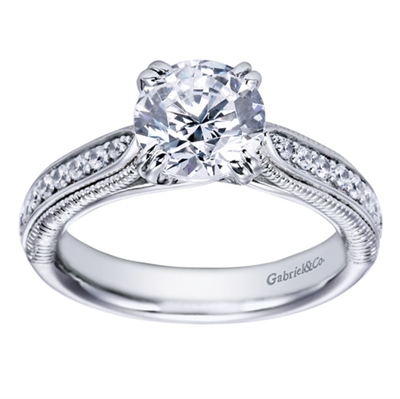 A round center diamond sits serenely at the center of this well decorated vintage styled engagement ring available in 18K white gold.