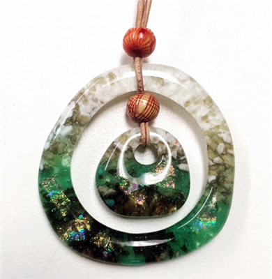 Two fused glass pendants strung together. The larger is an open circle. Strung inside is a smaller, solid circle. There is a wooden bead between them and a wooden bead above the larger pendant. The pendants are mainly green and white.