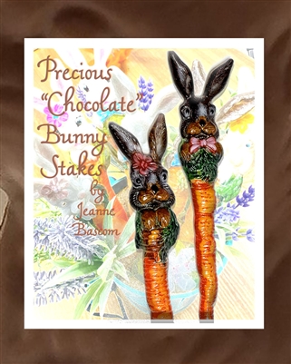 Two glass stakes placed on a background of semi-transparent flowers. The stakes are each topped by one brown rabbit and the stake itself is colored like a carrot. The background has the writing â€œPrecious â€˜Chocolateâ€™ Bunny Stakes by Jeanne Bascom.â€