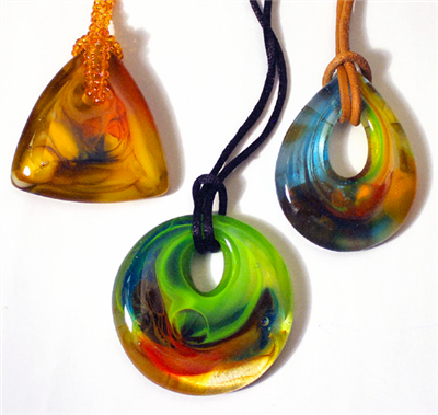 Three glass pendants strung with thick cord. The left is a triangle, the middle a circle, and the right a tear. Each pendant has different colors of glass swirled together. The triangle is yellowish, the circle green and blue, and the tear blue and yellow