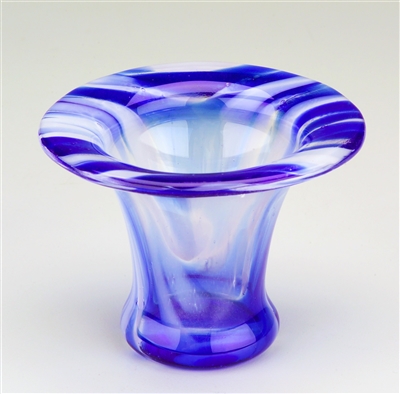 A glass vase on a light grey background. The glass is dark blue and white striped. The top portion of the vase was formed on a ring and the body formed through the glass dropping through the ring during firing.