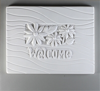 A rectangular tile made of white ceramic with a carved design. The center has a smaller rectangle filled with three daisy-like flowers and leaves. Below the flowers is curving text saying Welcome. The rest of the tile is filled with gentle waving lines.