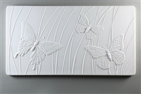 A long rectangular tile made of white ceramic. The carved texture on it shows three butterflies in front of a background of curving lines suggesting grass. Two of the butterflies are larger in the foreground, and there is one smaller one between them.