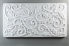 A long rectangular tile made of white ceramic. The carved texture is filled with curving lines with holly leaves and small round holly berries attached at various points.