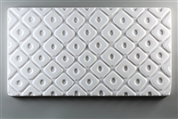 A long rectangular tile made of white ceramic. The carved texture is filled with a repeating pattern of diamonds. The diamonds are raised while the lines between them are carved. Each diamond has a small oval carved in its middle.