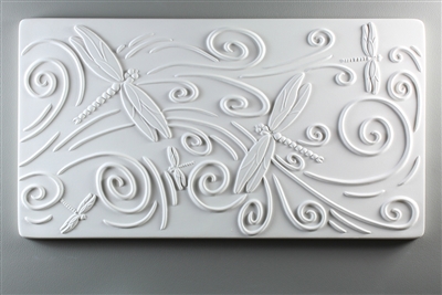 A long rectangular tile made of white ceramic. The carved texture has five dragonflies of various sizes in various places on the tile surrounded with curling lines. The curling lines suggest movement across the tile from left to right.