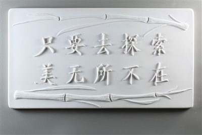 A long rectangular tile made of white ceramic. The carved texture has Chinese characters in the middle with two stalks of bamboo bordering them, one above and one below. The text roughly translates to beauty is everywhere as long as you look for it.