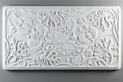 A long rectangular tile made of white ceramic. The carved texture is filled with flowers, fines, and leaves, and the entire tile has a delicate, curving, art nouveau-inspired border.