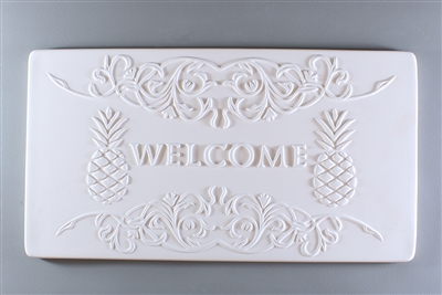 A long rectangular tile made of white ceramic. The carved texture says Welcome in the center. The word is flanked on either side by a pineapple, and the bottom and top of the tile have elaborate curving lines drawing attention inwards to the word.