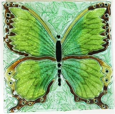 A decorative glass square showing a large butterfly design. The butterfly has a black body and head, and the wings are several shades of green with dark brown and amber outlines. The background is a lighter shade of green with a leaf pattern.