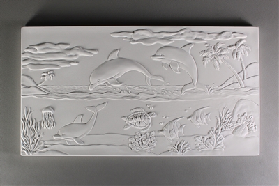 A long rectangular tile made of white ceramic. The carved texture shows a seascape. There are three dolphins playing in the center, with one visible below water. Various other fish are underwater, and two islands with palm trees flank either side.