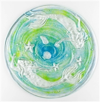 A top-down view of a clear glass dish with a mermaid design. The glass is clear. The two mermaids swimming around the edges of the dish are also clear, but the space between them has been filled with a swirl of teal and light green.