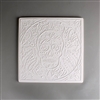A large square tile made of white ceramic. The carved texture shows a human skull in the center decorated in the style of the Day of the Dead. A circle of similar designs surrounds the skull with a square of simpler designs around it.