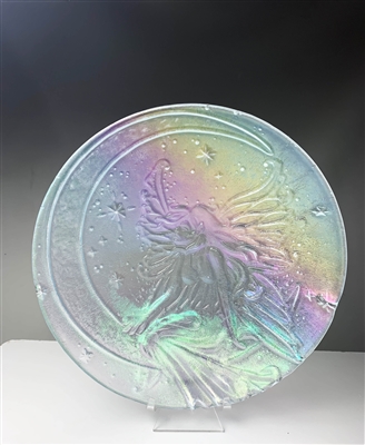 A clear glass circle displayed on a stand in front of a dark background. The circle has the design of a fairy sitting on a crescent moon embossed on it, and the entire glass piece has an iridescent sheen to it.