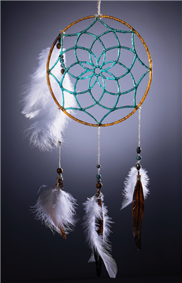 A glass dreamcatcher glass with glass feathers spotlit on a dark background. The glass feathers are brown, accented with real white feathers, and attached with beads and string. The dreamcatcher has teal strings and brown rim and its own feather accent.