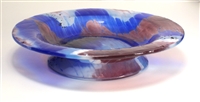 A footed glass dish on a white background. The glass has a wavy pattern of burgundy, bright blue, and light blue that have been lightly dragged into one another to create a flame stitch pattern on the dish.