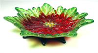 A footed glass dish. The dish itself is made from a frit cast poinsettia flower with yellow center and petals with bright red bases and light green tips. The feet of the dish are formed from dark green frit cast leaves.
