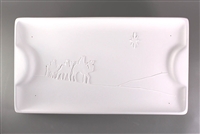 A rectangular white ceramic mold for fusing glass on a grey background. The edges are slightly raised, with a raised half circle at either end. The center has been carved with a desert landscape and the shadows of three men on camels looking to a star.