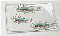 A rectangular dish made from fused glass. It is mostly clear glass that has been textured with the design of three simple fish. The fish have been filled in with light yellow fins and bellies, blue backs, and a magenta stripe in the middle.