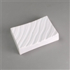A rectangular white ceramic mold for fusing glass on a grey background. Each corner curves slightly upwards. The mold has been carved with a repeating pattern of slightly waved lines going diagonally across.