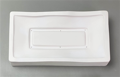 A long rectangular white ceramic mold for fusing glass on a grey background. The outside border is raised and cut into a waving shape. The border then slopes downward into a carved smaller rectangle outline with raised center.